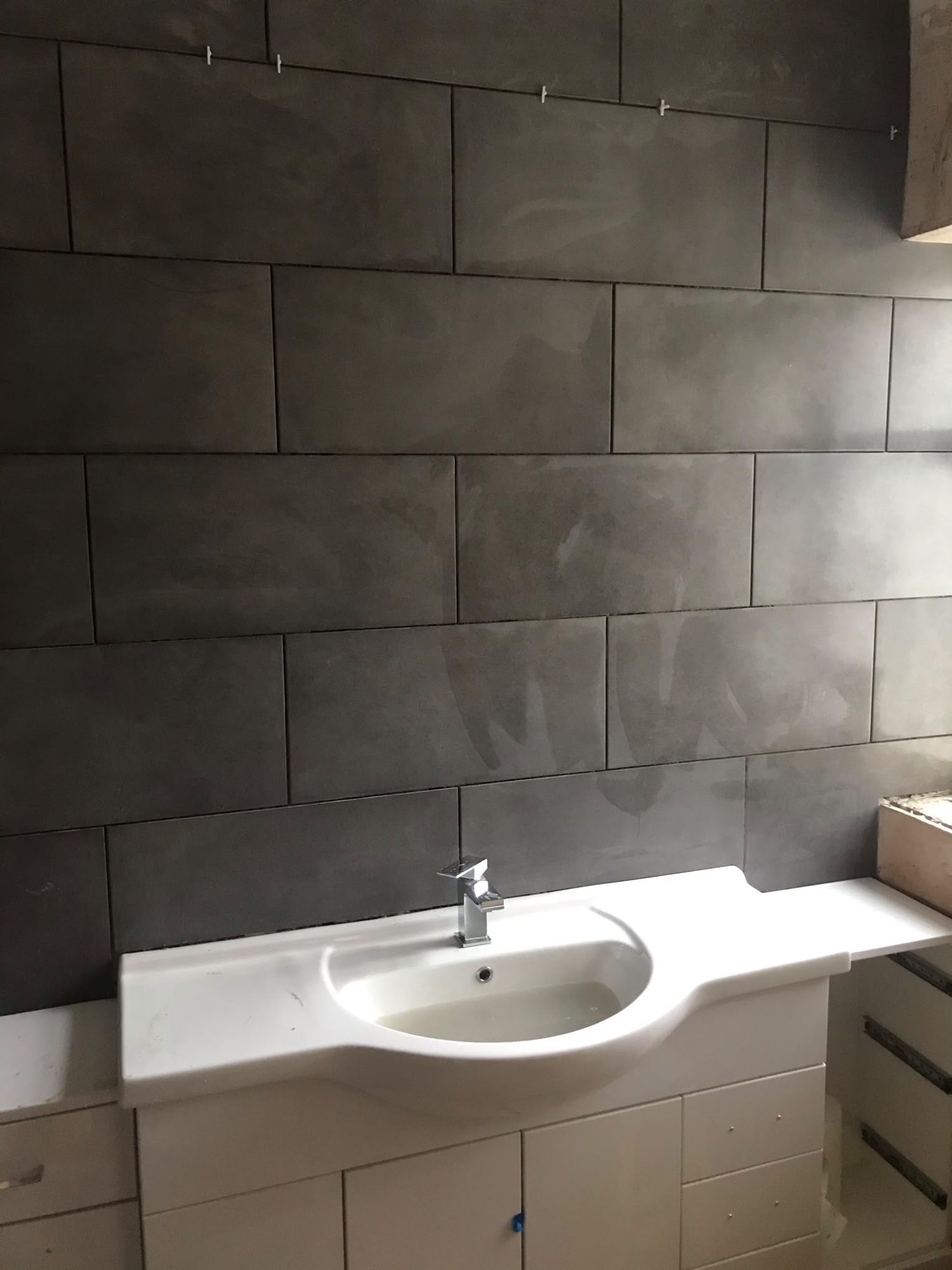 White vanity basin beneath grey bathroom wall tiles