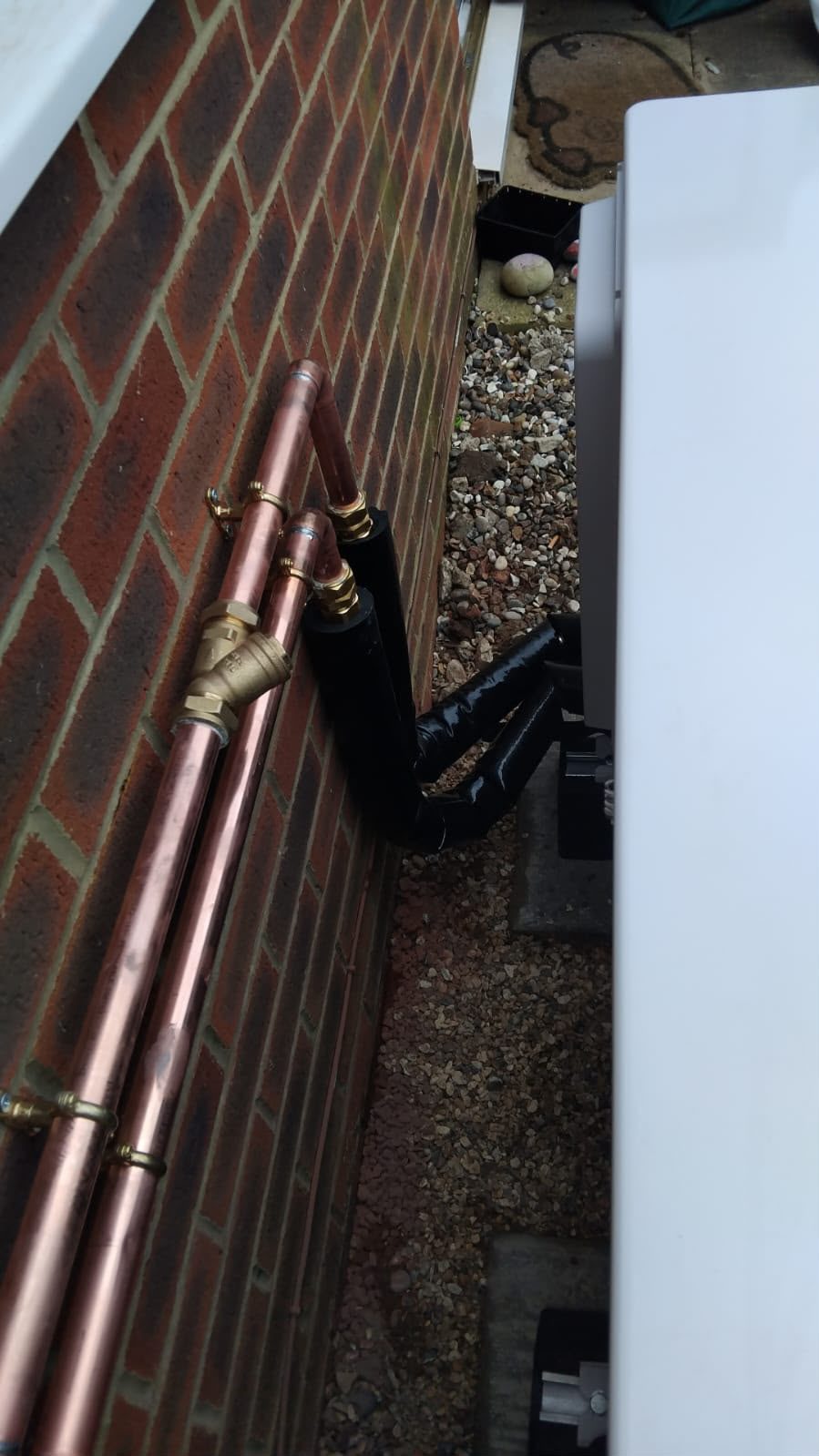 External insulated heating pipework beside a brick wall